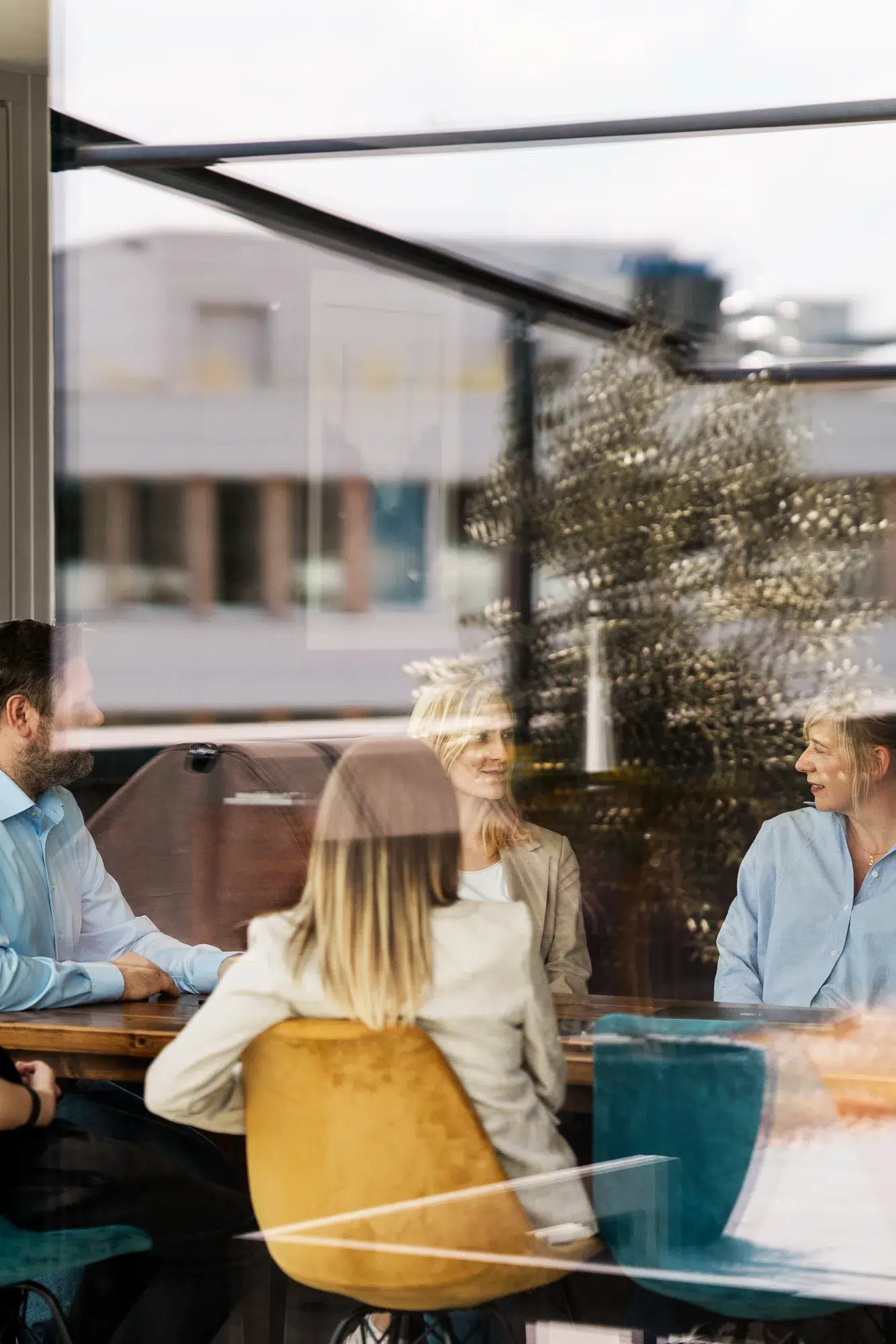 Teambesprechung an einem großen Tisch, von außen durch die Fensterscheibe fotografiert